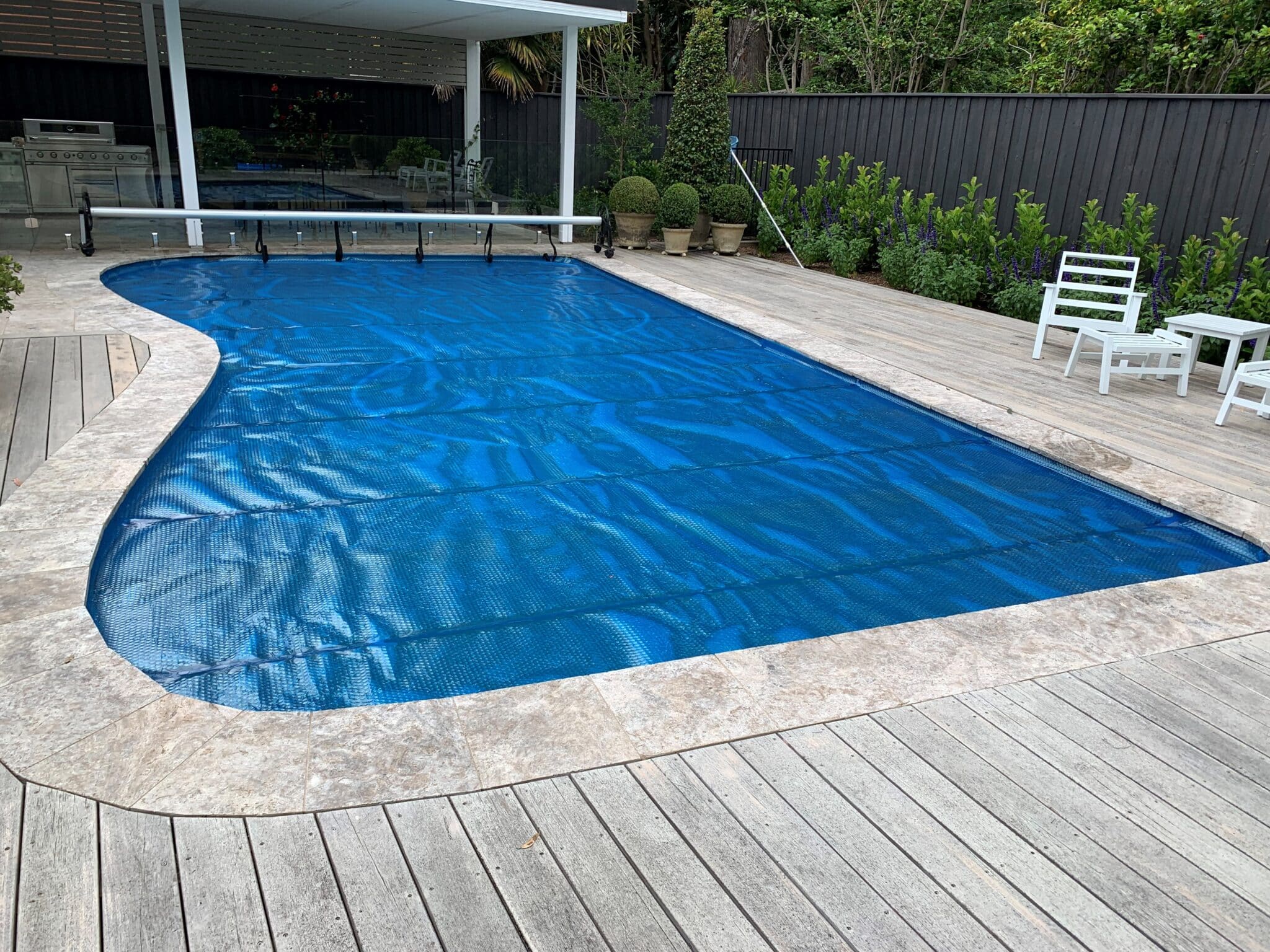 Blue thermal pool cover on a reel beside an inground pool